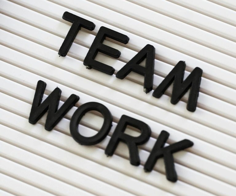 Schriftzüge „TEAM WORK“ in schwarzen Buchstaben auf einem hellen Hintergrund.